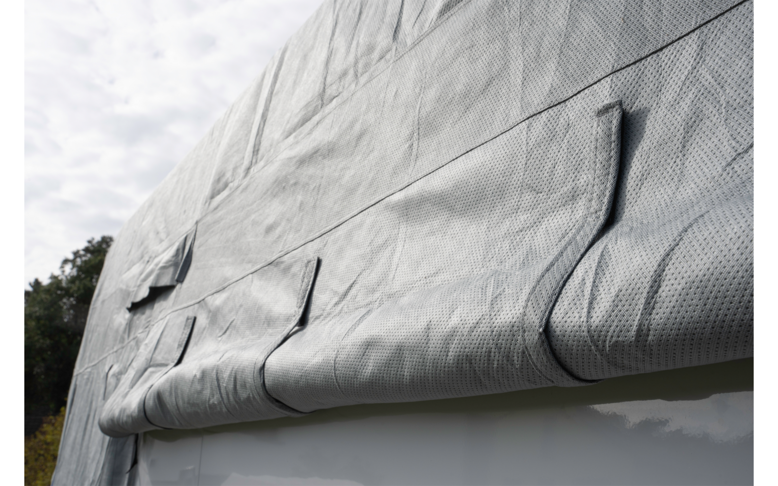 Gray, folded, textured fabric draped over a white smooth edge; trees on the left, cloudy sky above