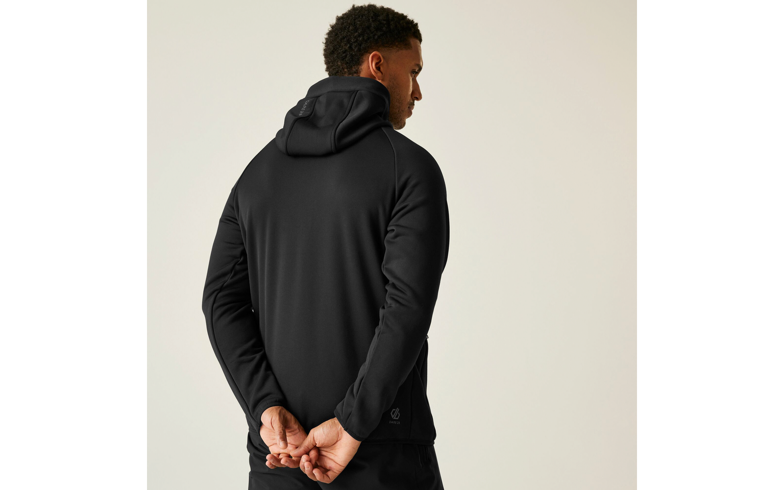 Ein Mann mit schwarzem Kapuzenpullover, von hinten, Hände hinter dem Rücken verschränkt