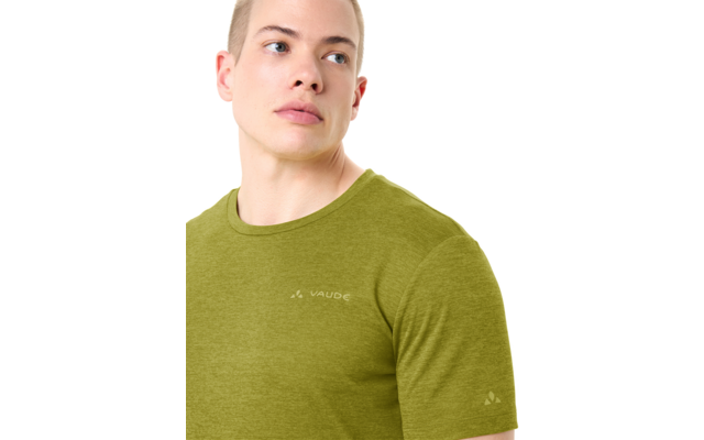 Persoon van borst omhoog, kijkt naar rechts, kort blond haar, draagt een olijfgroen T‑shirt met ronde hals en het "Vaude"-logo op borst en mouw, witte achtergrond