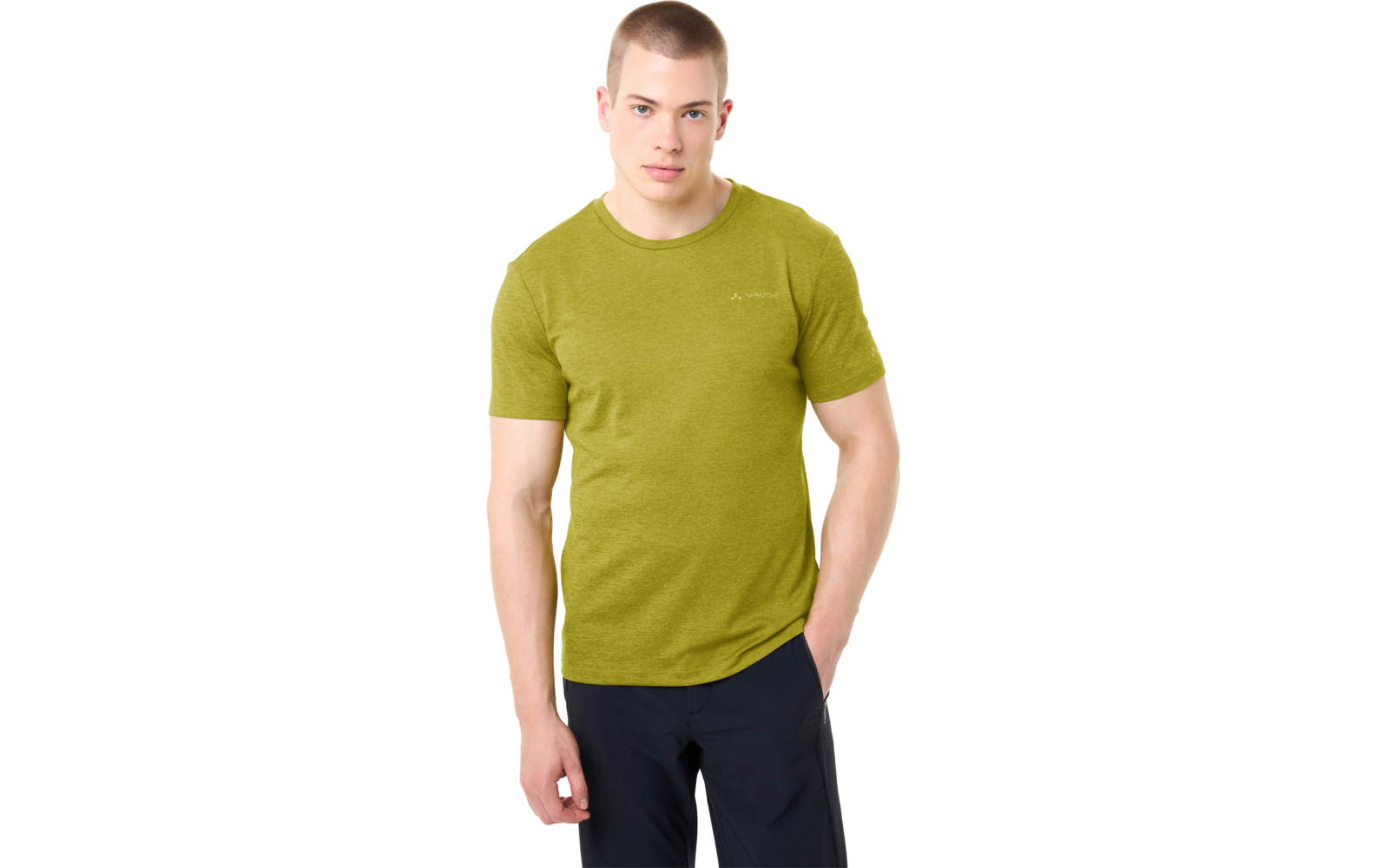 Staande persoon met kort haar, groen T-shirt en donkere broek, één hand in de zak, andere hand naast het lichaam, witte achtergrond