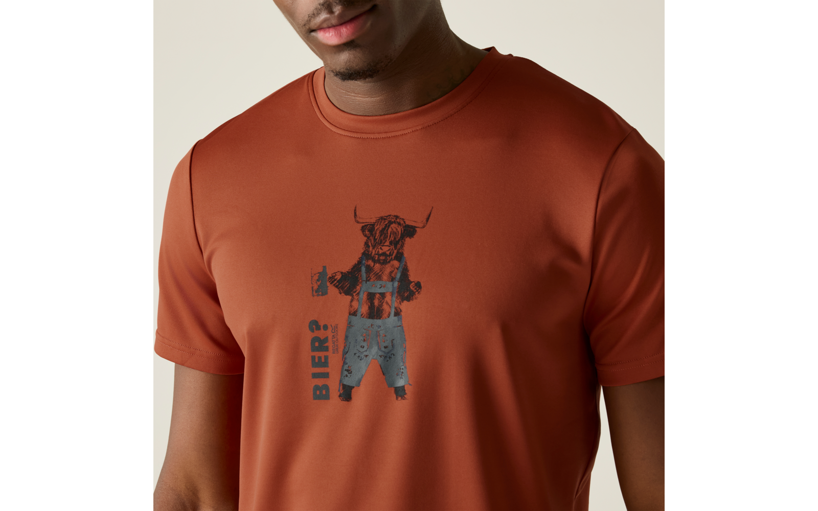 Oberkörper einer Person in rostfarbenem T-Shirt mit aufgedrucktem Stier in Latzhose, der ein Bierglas hält; daneben steht senkrecht 'BIER?'