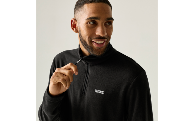 Man with short hair and beard wearing a black fleece pullover pulls the zipper and looks to the side
