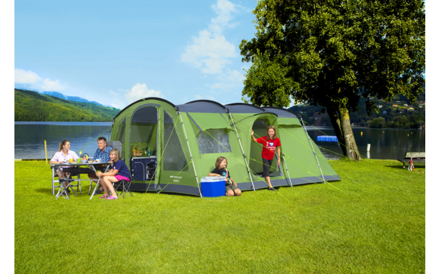 Familie mit Zelt und Campingstuhl auf einer Wiese am See