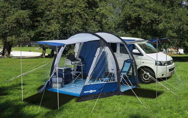 Tenda da campeggio con tettoia aperta accanto a un camper bianco su prato verde