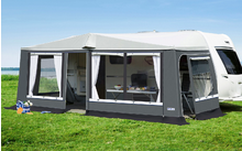 Telo grigio attaccato a una roulotte bianca su erba verde sotto un cielo blu