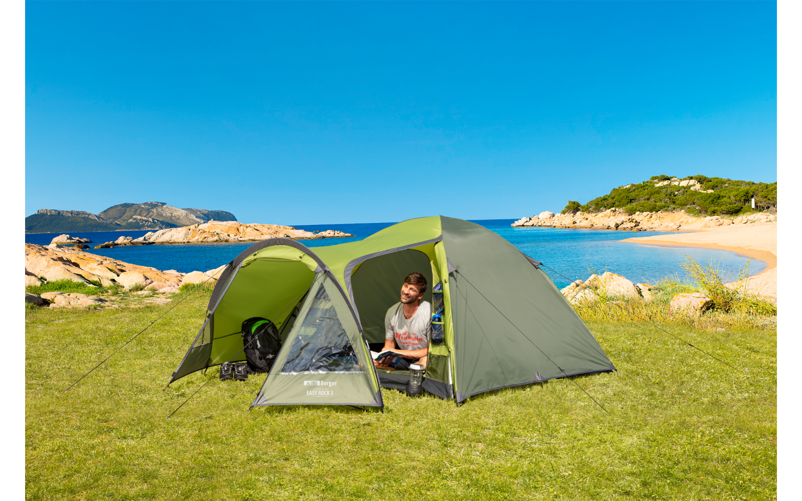 Grüne Zelt auf einer Wiese am Meer, eine Person sitzt vor dem Zelt