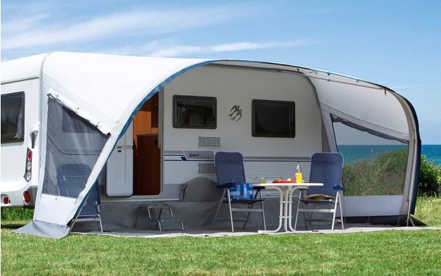 Camping-car avec auvent attaché sur une pelouse verte sous un ciel bleu