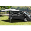 Schwarzer Campervan mit ausgefahrenem grauen Sonnenschutz auf einer grünen Wiese, im Hintergrund Bäume