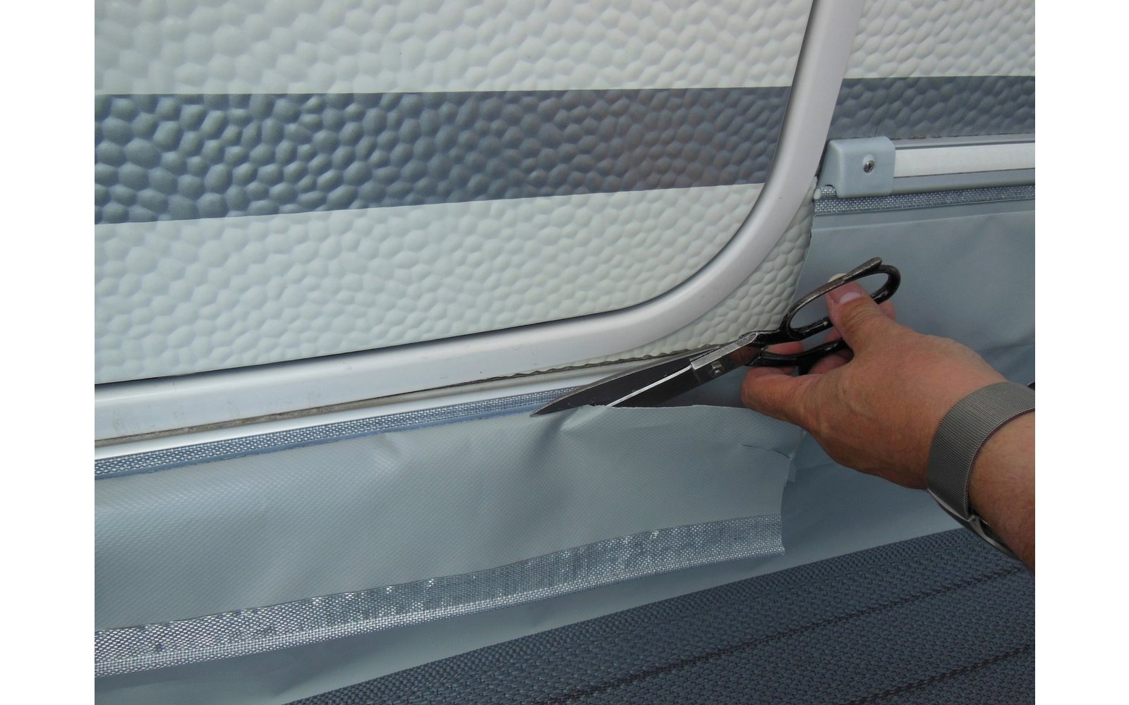 Hand hält ein Werkzeug und schneidet eine Dichtungsfolie an einer Fensterkante