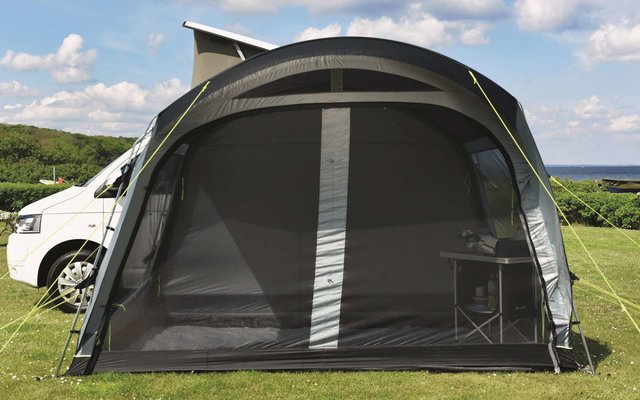 Aufblasbares Vorzelt neben einem weißen Wohnmobil auf einer Wiese unter blauem Himmel mit Wolken