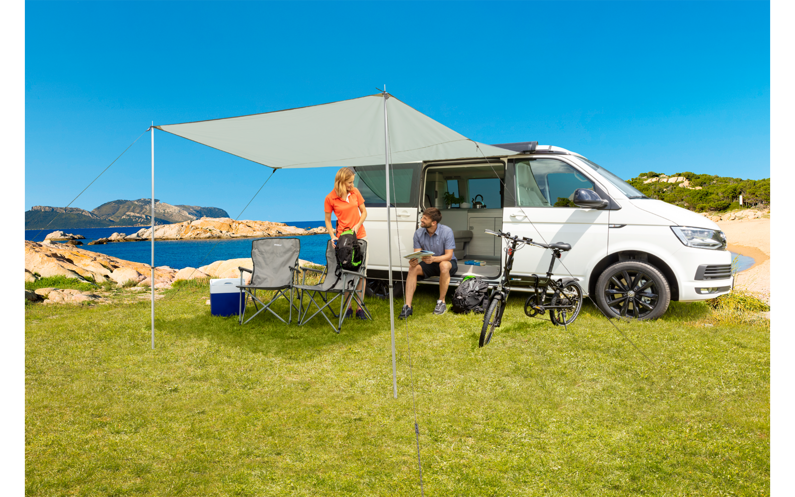 Camping-car avec auvent déployé et deux personnes assises à l'extérieur
