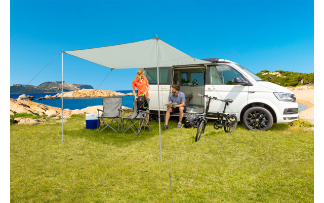 Camping-car avec auvent déployé et deux personnes assises à l'extérieur