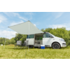 Camping-car blanc avec auvent déployé stationné sur un champ herbeux sous un ciel bleu