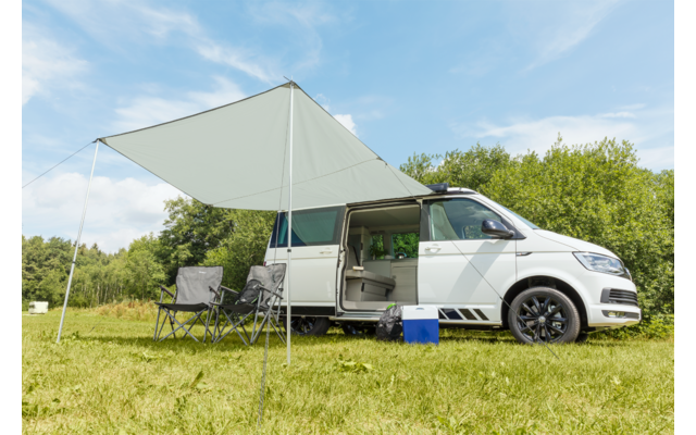 Camping-car blanc avec auvent déployé stationné sur un champ herbeux sous un ciel bleu