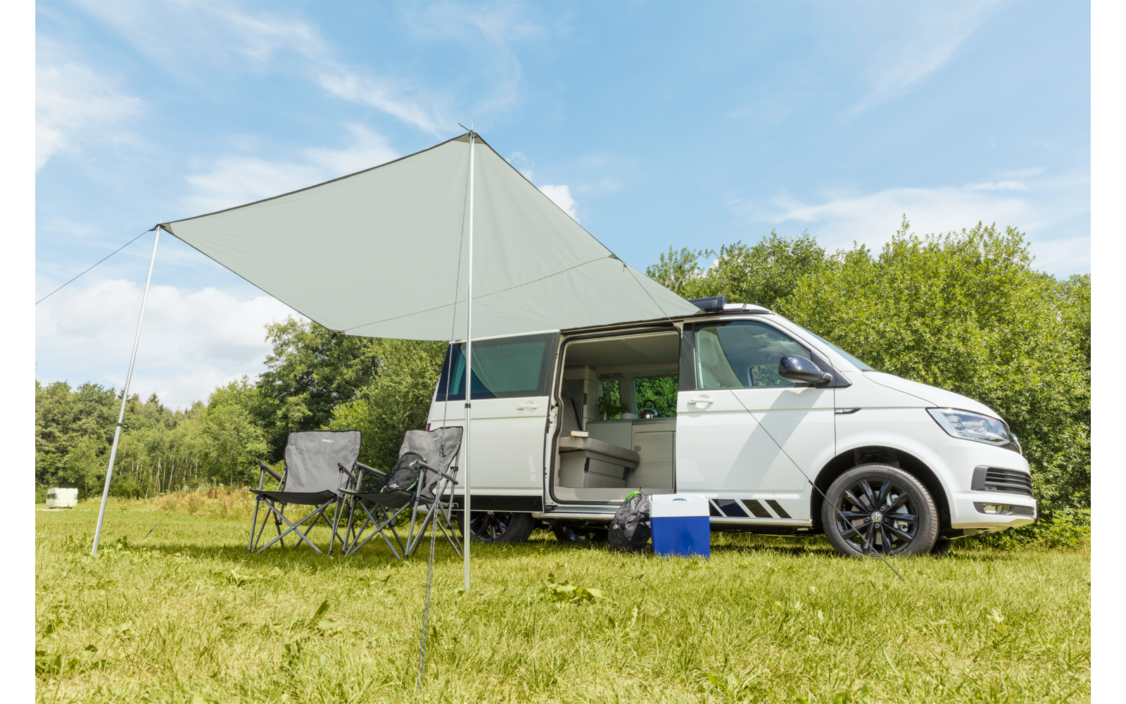 Camping-car blanc avec auvent déployé stationné sur un champ herbeux sous un ciel bleu