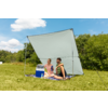 Trois personnes assises sur l'herbe sous un grand parasol blanc