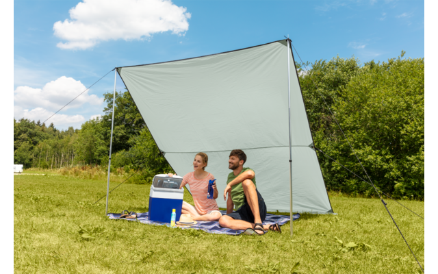Trois personnes assises sur l'herbe sous un grand parasol blanc
