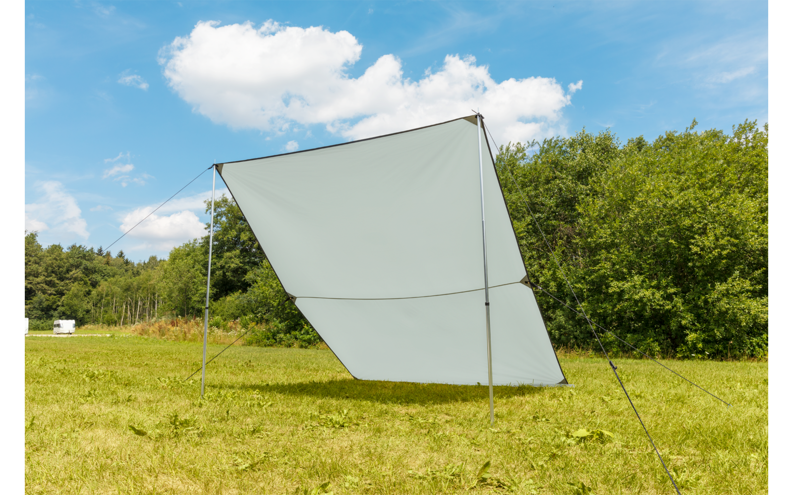 Une voile d'ombrage blanche sur une prairie verte sous un ciel bleu avec quelques nuages