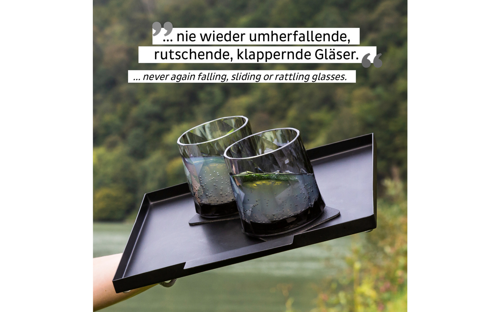 Drei Gläser mit Getränk auf einem schwarzen Tablett vor grüner, unscharfer Landschaft