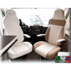 Interior eines Wohnmobils mit zwei Vorderfahrersitzen, einer in Weiß und einer in Beige, und einem Tisch links im Bild