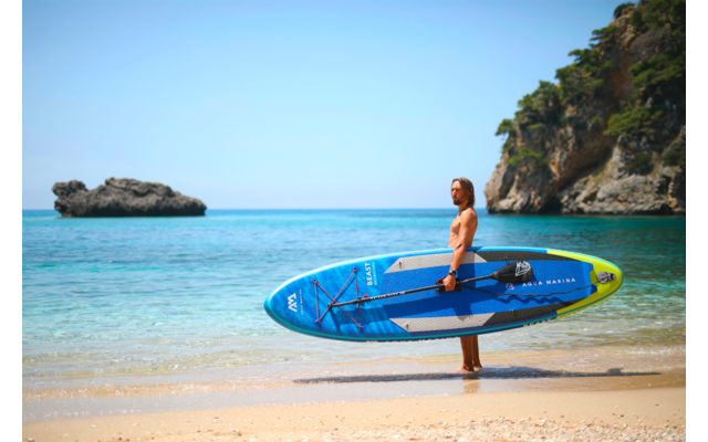 Frau am Strand mit blauem Stand-Up-Paddle-Board neben dem Wasser