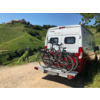 Wohnmobil mit zwei Fahrrädern auf Fahrradträger, im Hintergrund grüne Hügel und ein Zaun