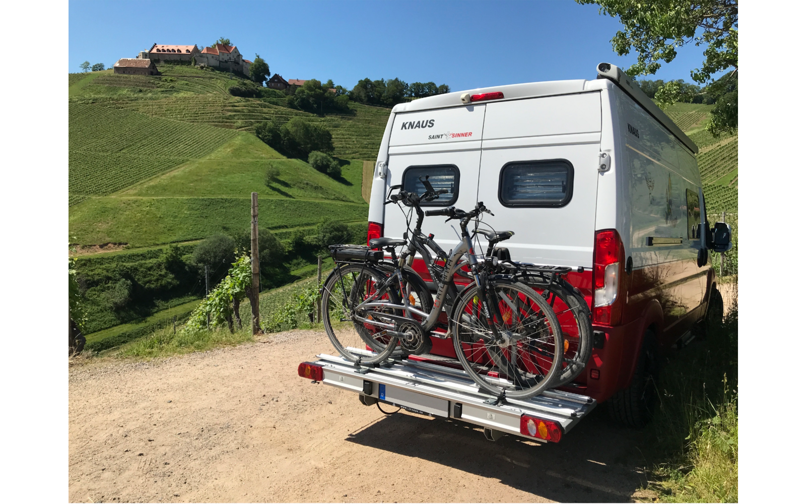 Wohnmobil mit zwei Fahrrädern auf Fahrradträger, im Hintergrund grüne Hügel und ein Zaun