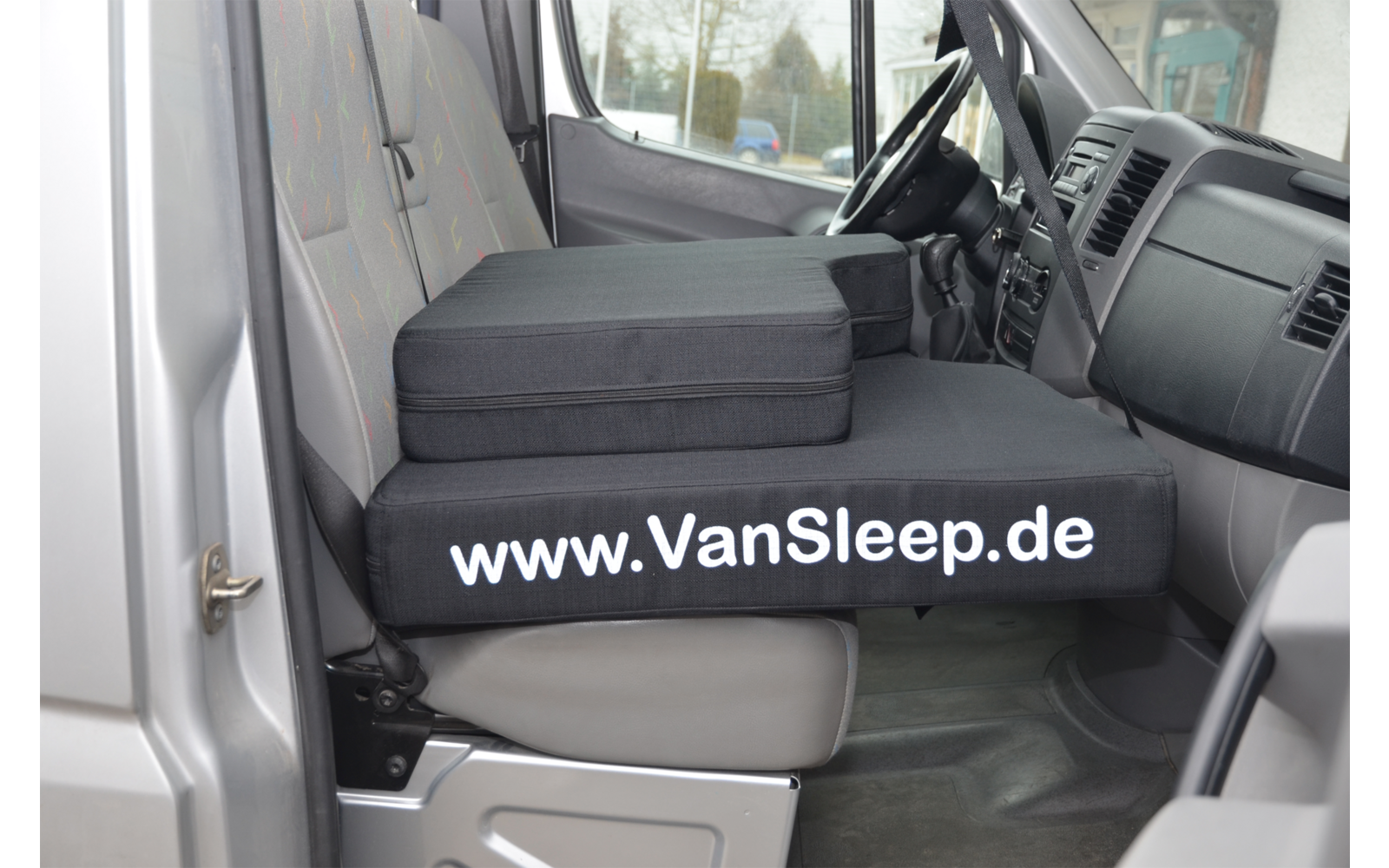 Innenraum eines Fahrzeugs mit einem Sitz umgebaut als Schlafplatz mit der Aufschrift www.VanSleep.de