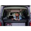 Woman sitting in the open trunk of a vehicle, looking at a tablet