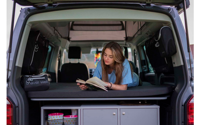 Woman sitting in the open trunk of a vehicle, looking at a tablet