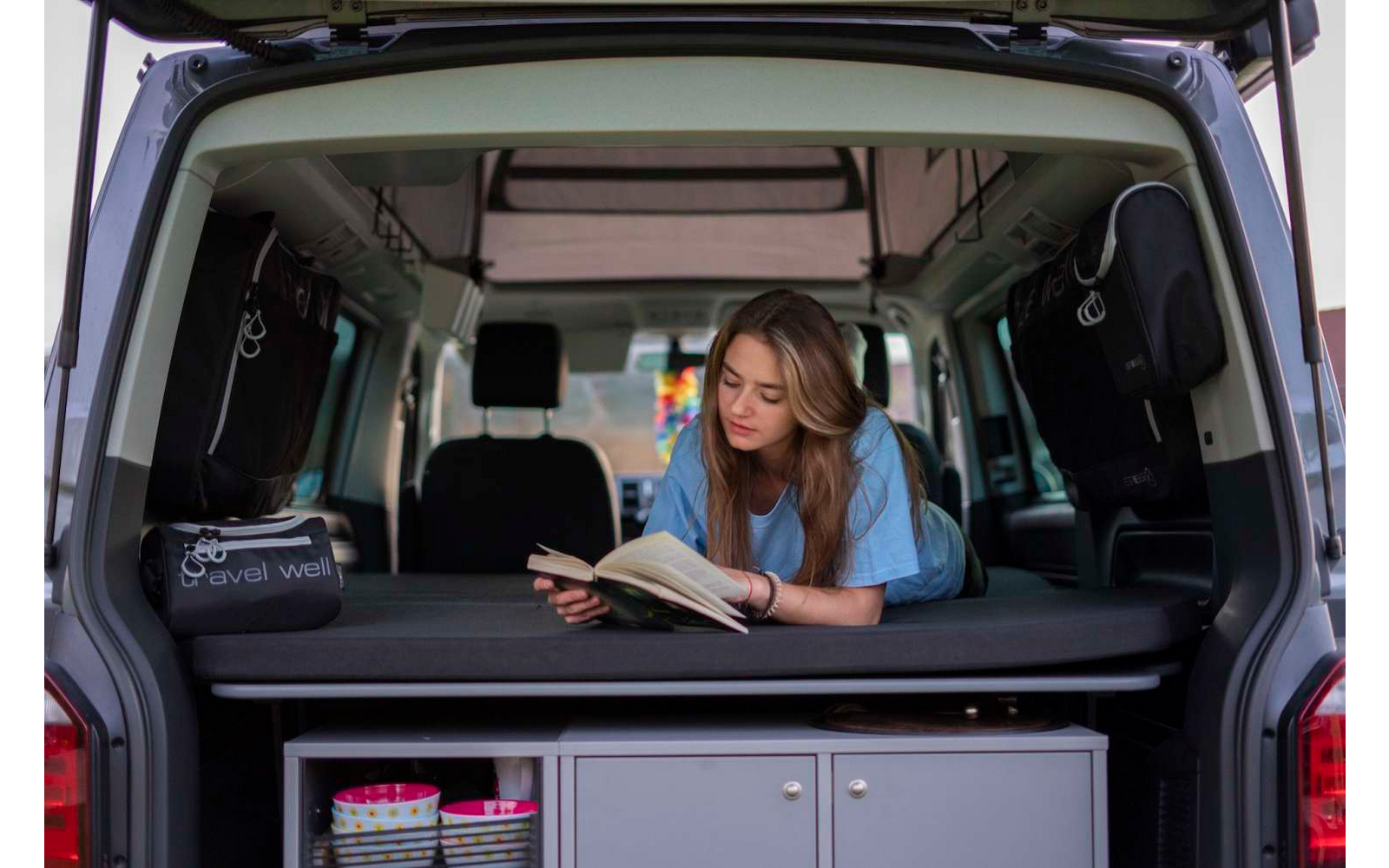 Woman sitting in the open trunk of a vehicle, looking at a tablet