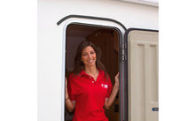 Vrouw in rood poloshirt staat in de open deur van een voertuig