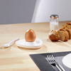 Boiled egg in white egg cup, knife, salt shaker, and bread on wooden table