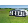 Caravan with attached bright awning on a green meadow in front of a lake and blue sky