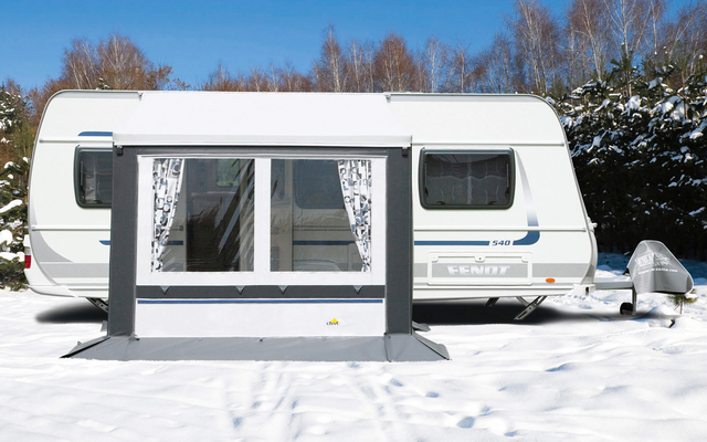 Witte caravan staat op met sneeuw bedekte grond met kale bomen op de achtergrond