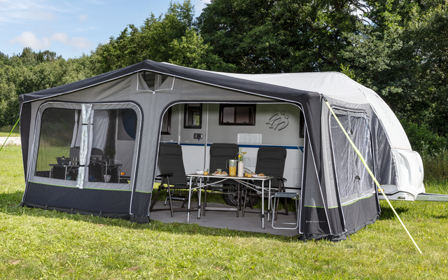 Large gray awning with open windows and a table with chairs in front, on green grass, trees in the background