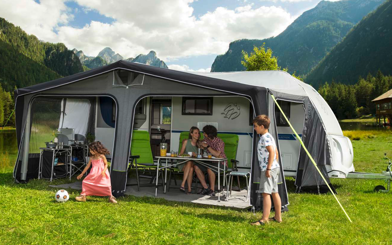 Family with children in front of a caravan in a green mountain landscape