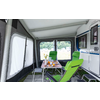 Interior of a modern camper with a white table, green chairs, and large windows