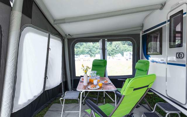 Interior of a modern camper with a white table, green chairs, and large windows