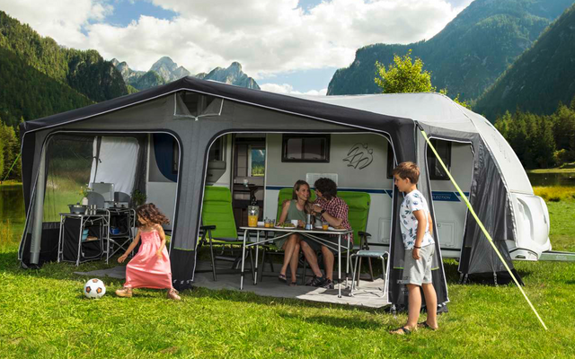 Family with two children in front of a caravan on a green meadow in the mountains under a cloudy sky