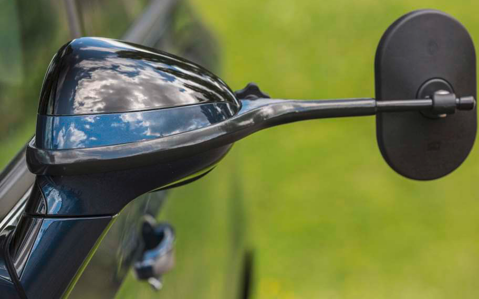 Nahaufnahme eines schwarzen Motorradspiegels und eines Teils des Lenkers vor unscharfem grünem Hintergrund