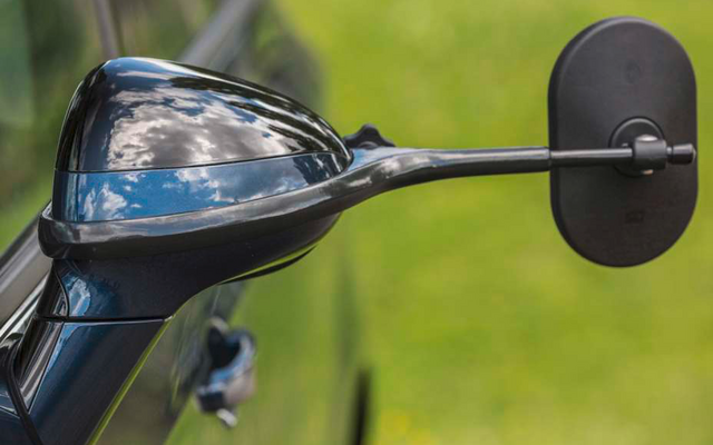 Nahaufnahme eines schwarzen Motorradspiegels und eines Teils des Lenkers vor unscharfem grünem Hintergrund