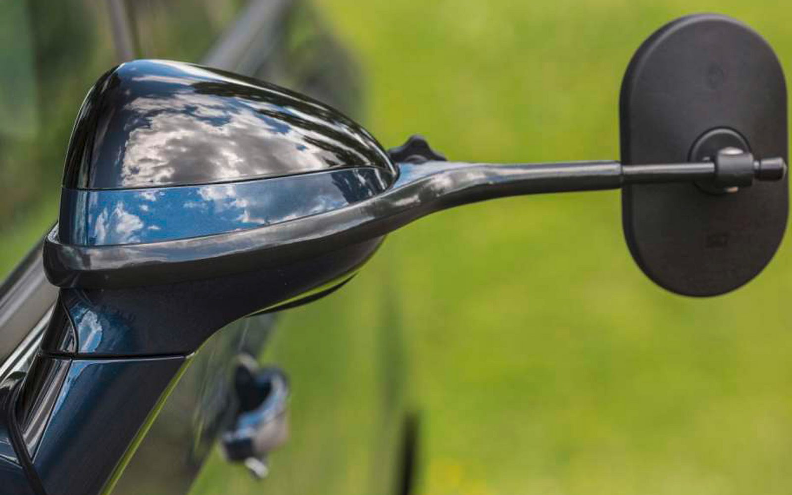 Nahaufnahme eines schwarzen Motorradspiegels und eines Teils des Lenkers vor unscharfem grünem Hintergrund