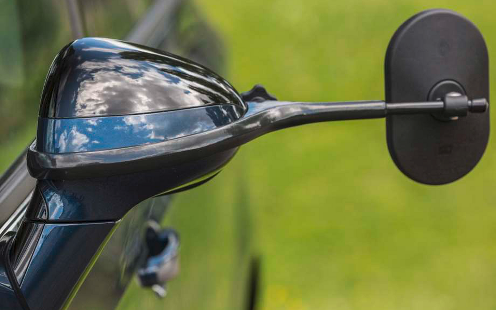 Nahaufnahme eines schwarzen Motorradspiegels und eines Teils des Lenkers vor unscharfem grünem Hintergrund