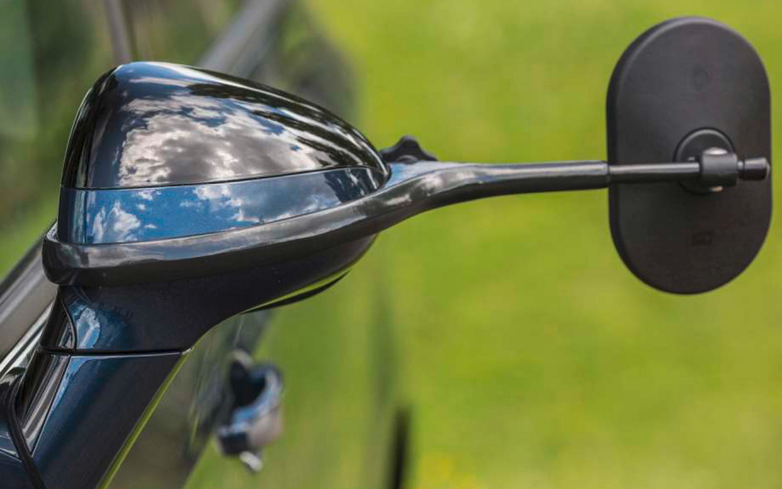 Nahaufnahme eines schwarzen Motorradspiegels und eines Teils des Lenkers vor unscharfem grünem Hintergrund