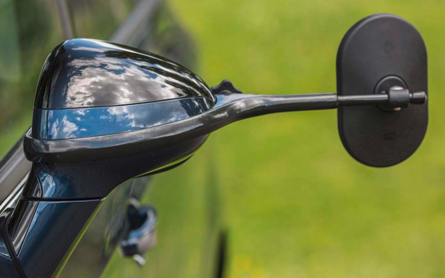 Nahaufnahme eines schwarzen Motorradspiegels und eines Teils des Lenkers vor unscharfem grünem Hintergrund