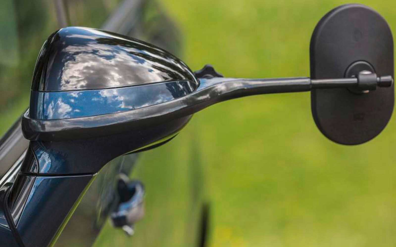 Nahaufnahme eines schwarzen Motorradspiegels und eines Teils des Lenkers vor unscharfem grünem Hintergrund