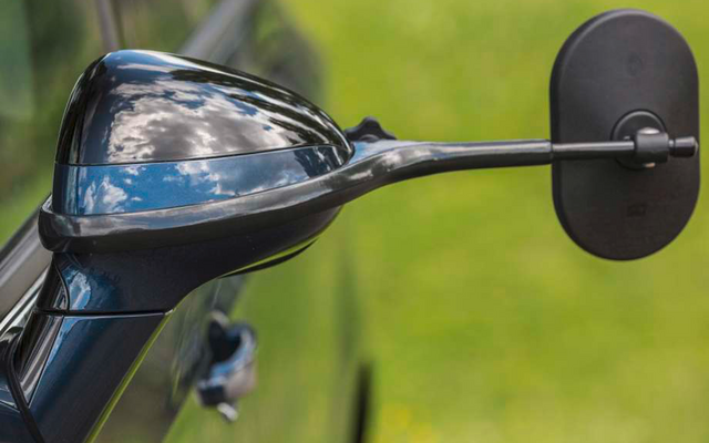 Nahaufnahme eines schwarzen Motorradspiegels und eines Teils des Lenkers vor unscharfem grünem Hintergrund