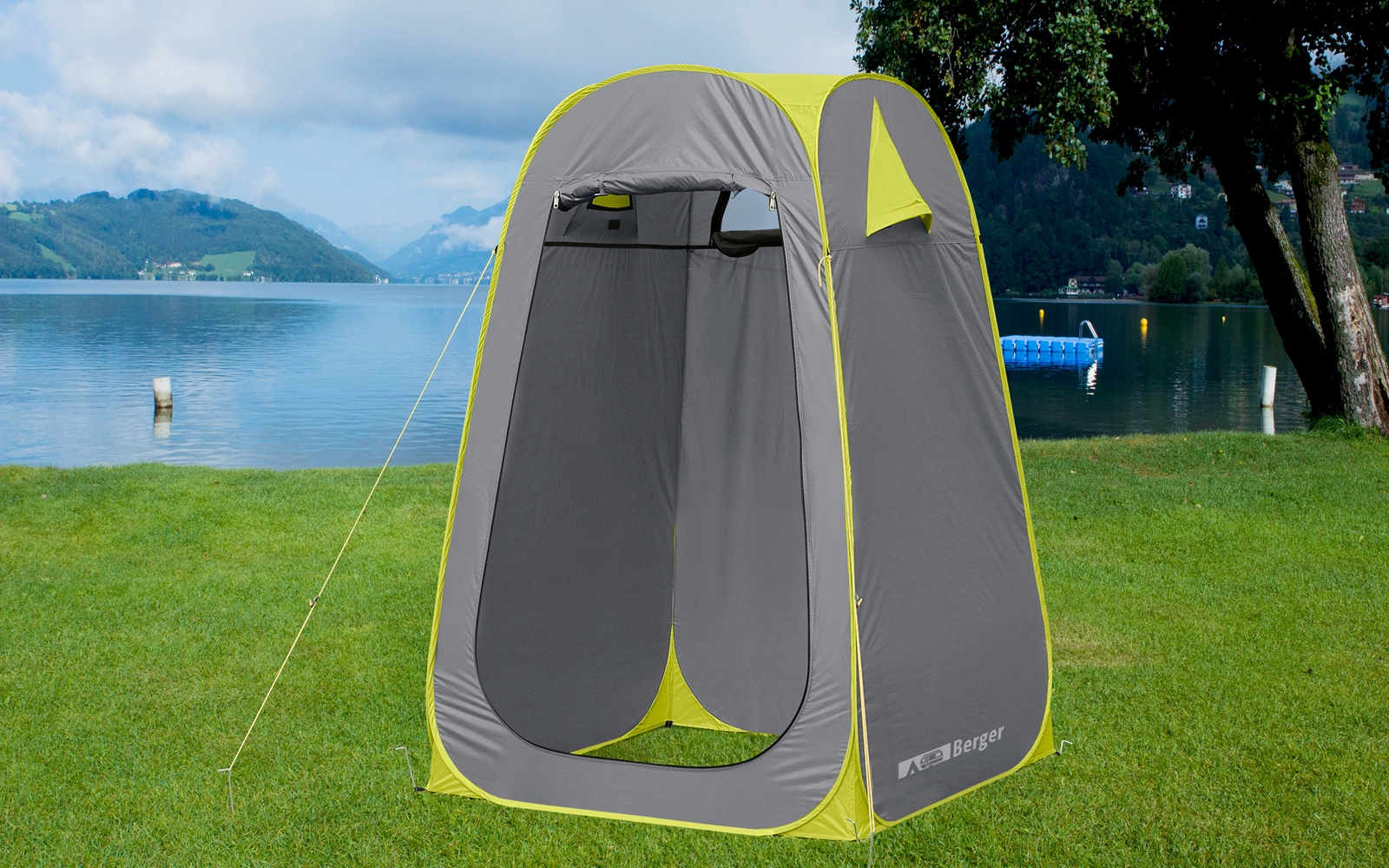 Ein graues und gelbes Pop-up-Zelt steht auf einer grünen Wiese neben einem See mit Bergen im Hintergrund