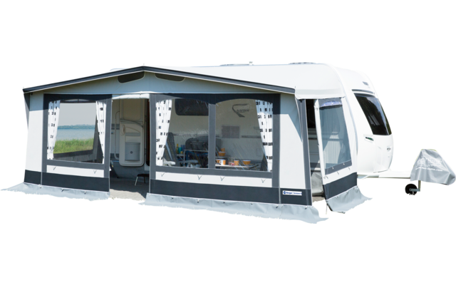 Caravan with attached awning on a green meadow under a blue sky